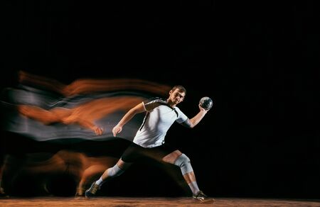 Caucasian young handball player in action and motion in mixed lights over black studio background. Fit male professional sportsman. Concept of sport, movement, energy, dynamic, healthy lifestyle.の写真素材