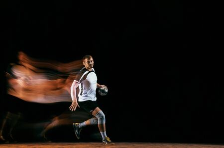 Caucasian young handball player in action and motion in mixed lights over black studio background....