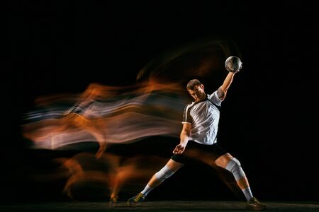 Caucasian young handball player in action and motion in mixed lights over black studio background. Fit male professional sportsman. Concept of sport, movement, energy, dynamic, healthy lifestyle.の写真素材
