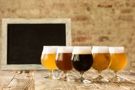 Glasses of different kinds of dark and light beer on wooden table in line. Cold delicious drinks...