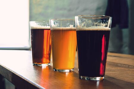 Glasses of different kinds of dark and light beer on wooden table in line. Cold delicious drinks are...
