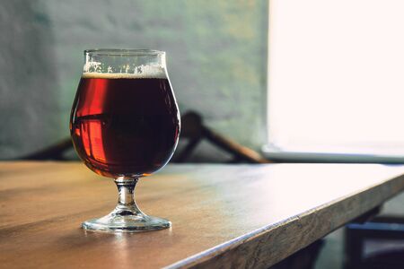 Glass of dark beer on wooden table against brick background. Cold delicious drink is prepared for a...