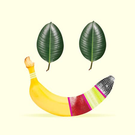 Nature's smile. Banana and green leaves as a human emotion of happiness on yellow background. Negative space. Modern design. Contemporary art. Creative conceptual and colorful collage.の写真素材
