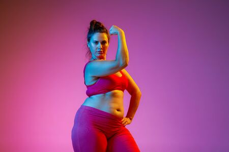 Young caucasian plus size female models doing exercises on gradient purple background in neon light....