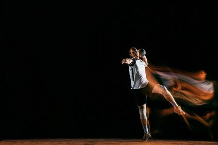 Caucasian young handball player in action and motion in mixed lights over black studio background. Fit male professional sportsman. Concept of sport, movement, energy, dynamic, healthy lifestyle.の写真素材