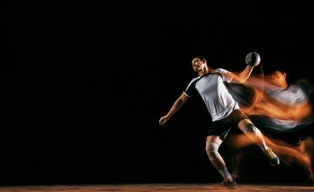 Caucasian young handball player in action and motion in mixed lights over black studio background. Fit male professional sportsman. Concept of sport, movement, energy, dynamic, healthy lifestyle.の写真素材