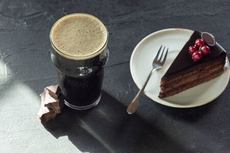 Glass of dark beer on the stone table background. Cold drink and truffles with cake are prepared for a big friends party. Concept of drinks, fun, food, celebrating, meeting, oktoberfest.の写真素材