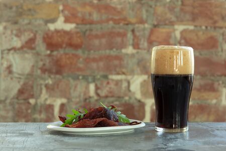 Glass of dark beer on the stone table and bricks background. Cold drink and meat snacks are prepared for a big friends party. Concept of drinks, fun, food, celebrating, meeting, oktoberfest.の写真素材
