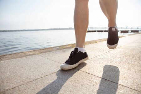 Senior man as runner with armband or fitness tracker at the riverside. Caucasian male model practicing jogging and cardio trainings in summers morning. Healthy lifestyle, sport, activity concept.の写真素材