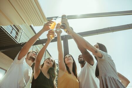 Young group of friends drinking beer, having fun, laughting and celebrating together. Women and men with beers glasses in sunny day. Oktoberfest, friendship, togetherness, happiness, summer concept.の写真素材