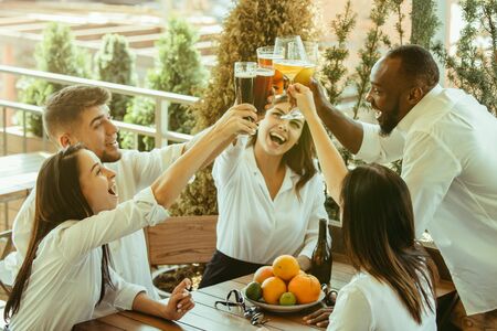 Young group of friends drinking beer, having fun, laughting and celebrating together. Women and men with beers glasses in sunny day. Oktoberfest, friendship, togetherness, happiness, summer concept.の写真素材