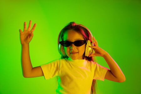 Beautiful female half-length portrait isolated on green backgroud in neon light. Young emotional teen girl in sunglasses. Human emotions, facial expression concept. Trendy colors. Dancing, smiling.の写真素材