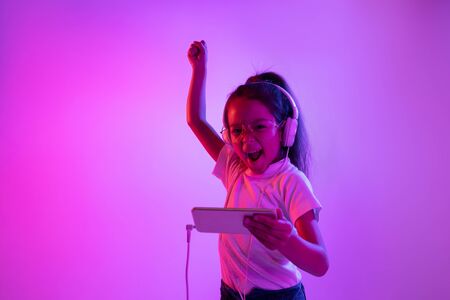 Beautiful female portrait isolated on purple backgroud in neon light. Emotional girl in eyeglasses....