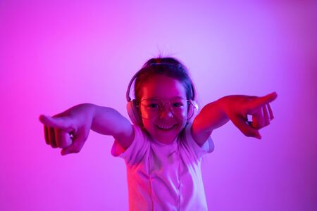 Beautiful female half-length portrait isolated on purple backgroud in neon light. Young emotional teen girl in eyeglasses. Human emotions, facial expression concept. Trendy colors. Dancing, pointing.の写真素材