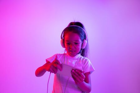 Beautiful female half-length portrait isolated on purple backgroud in neon light. Emotional girl in eyeglasses. Human emotions, facial expression concept. Dancing, listening to music, gaming.の写真素材