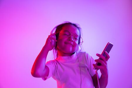 Beautiful female half-length portrait isolated on purple backgroud in neon light. Emotional girl in eyeglasses. Human emotions, facial expression concept. Dancing, listening to music, making selfie.の写真素材