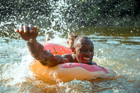 Happy man having fun while laughting and swimming in river. Joyful male models with rubber ring as a...