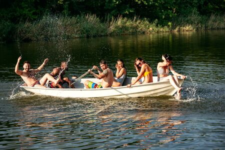 Happy group of friends having fun while laughting and swimming in river. Joyful men and women in...