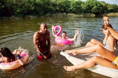 Happy group of friends having fun while laughting and swimming in river. Joyful men and women in...