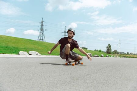 Skateboarder doing a trick at the citys street in sunny day. Young man in equipment riding and...