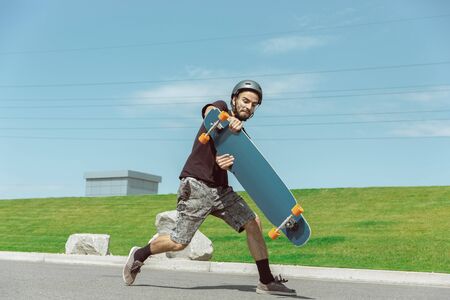 Skateboarder doing a trick at the citys street in sunny day. Young man in equipment riding and...