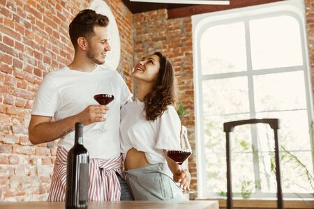 Young couple moved to a new house or apartment. Drinking red wine, caddling and relaxing after...