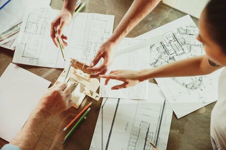 Top view of achitect-engineers hands shows future house, office or store design plans to a young couple. Meeting at the construction office to talk about facade, interior decoration, home layout.の写真素材