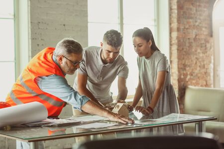 Foreman or achitect engineer shows future house, office or store design plans and model to a young couple. Meeting at the construction office to talk about facade, interior decoration, home layout.の写真素材