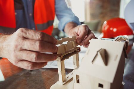 Close up photoshot of male architect-engineer making a model of future house for young family. Man...