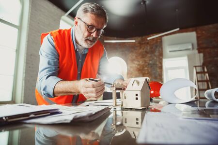 Close up photoshot of male architect-engineer making a model of future house for young family. Man...