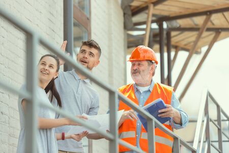 Foreman or achitect engineer shows future house, office or store design plans to a young couple....