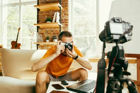 Young caucasian male blogger with professional equipment recording video review of camera at home. Blogging, videoblog, vlogging. Man making vlog or live stream about photo or technical novelty.の写真素材