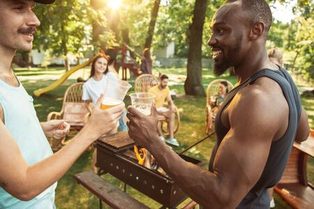Group of happy friends having beer and barbecue party at sunny day. Resting together outdoor in a...