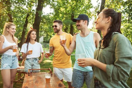 Group of happy friends having beer and barbecue party at sunny day. Resting together outdoor in a forest glade or backyard. Celebrating and relaxing, laughting. Summer lifestyle, friendship concept.の写真素材