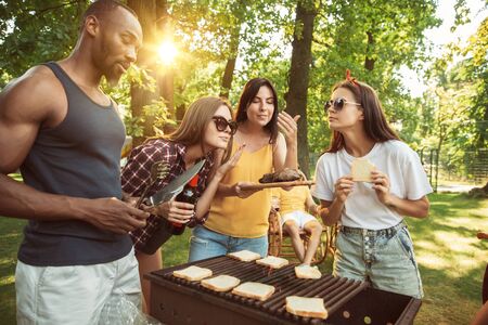 Group of happy friends having beer and barbecue party at sunny day. Resting together outdoor in a forest glade or backyard. Celebrating and relaxing, laughting. Summer lifestyle, friendship concept.の写真素材