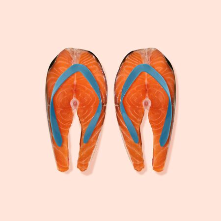 Lets go to the beach. Slippers as a salmon steaks on coral background. Negative space to insert your text. Modern design. Contemporary art collage. Concept of summertime, holiday, resort.の写真素材