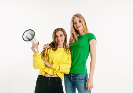 Young women weared in LGBT flag colors on white background. Caucasian models in bright shirts. Look happy, smiling and hugging. LGBT pride, human rights and choice concept. Holding mouthpiece.の写真素材