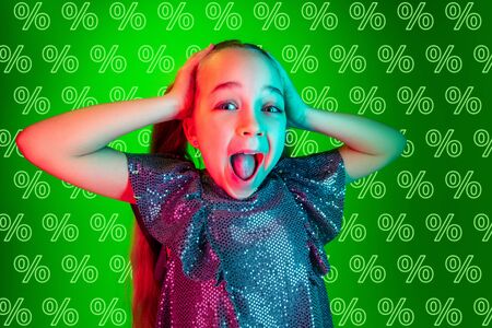 Portrait of young caucasian girl on green background with neon percents. Shocked, crazy happy, astonished. Concept of sales, black friday, cyber monday, finance, business. Online shops and payments bill.の写真素材