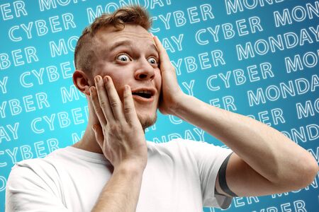 Portrait of young caucasian man on blue background with neon lettering. Shocked, astonished. Concept of sales, black friday, cyber monday, finance, business. Online shops and payments bill.の写真素材