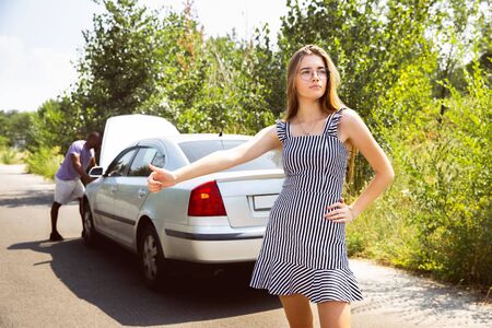Young multiethnic couple broke down the car while traveling on the way to rest. They are trying to...