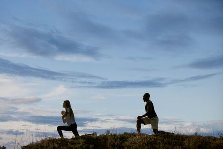 Young multiethnic international couple outdoors at the meadow in evening on sky background. African-american man and caucasian woman training and practicing together. Sport, recreation, lifestyle.の写真素材