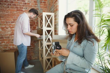 Build the future together. Young couple moved to a new house or apartment. Look happy and confident. Family, moving, relations, first home concept. Making photo, laughting while unpacking their things.の写真素材