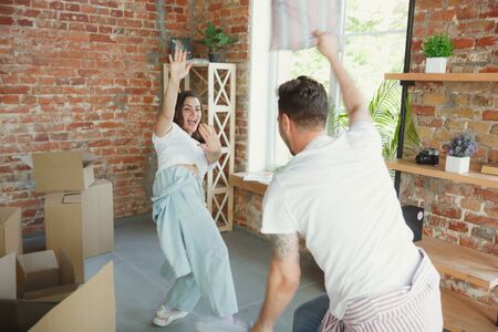 Happiness. Young couple moved to a new house or apartment. Look happy and confident. Family, moving, relations, first home concept. Have fun, laughting and dancing while unpacking their boxes.の写真素材