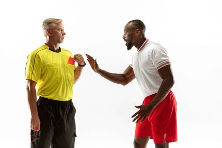 Referee showing a red card to a displeased african-american football or soccer player while gaming isolated on white background. Concept of sport, rules violation, controversial issues, emotions.の写真素材
