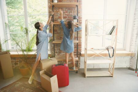 New life. Young mother and her daughter moved to a new house or apartment. Look happy and confident. Moving, relations, lifestyle concept. Playing together, unpacking things and laughting.の写真素材