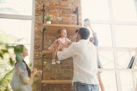 New life. Adult family moved to a new house or apartment. Spouses and children look happy and confident. Moving, relations, new life concept. Playing together, unpacking books and domestic plants.の写真素材