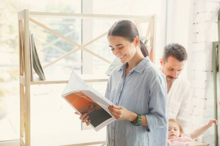 New life. Adult family moved to a new house or apartment. Spouses and children look happy and confident. Moving, relations, lifestyle concept. Unpacking boxes with their books, playing together.の写真素材