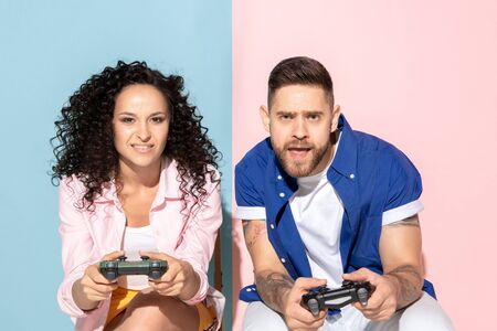 Young emotional caucasian couple in bright casual clothes posing on pink and blue background....