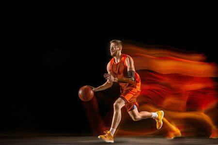 The comet. Young caucasian basketball player of red team in action and motion in mixed light over dark studio background. Concept of sport, movement, energy and dynamic, healthy lifestyle.の写真素材