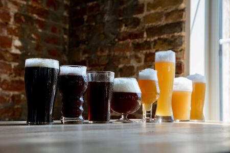 Glasses of dark and light beer and ale in sunlight on brick wall background. Cold delicious alcohol...